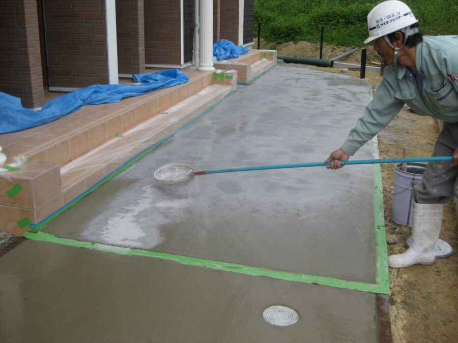 アパートのアプローチにカラーハードナーを均一に散布する工程（スタンプコンクリート）