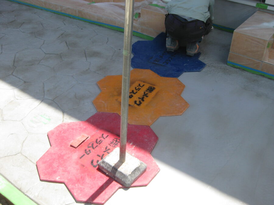 アパートアプローチのスタンプコンクリートにマットを押し当て模様を形成する様子